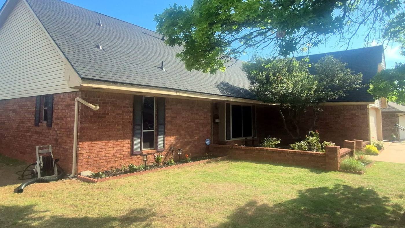 New dark gray architectural shingle roof on a brick ranch-style house under a clear blue sky
